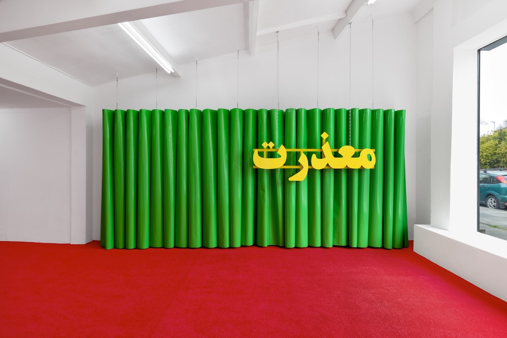 Sculpture featuring yellow acrylic Farsi text &ldquo;I&rsquo;m sorry&rdquo; against green plastic curtain, part of Nazanin Noori’s exhibition at Auto Italia